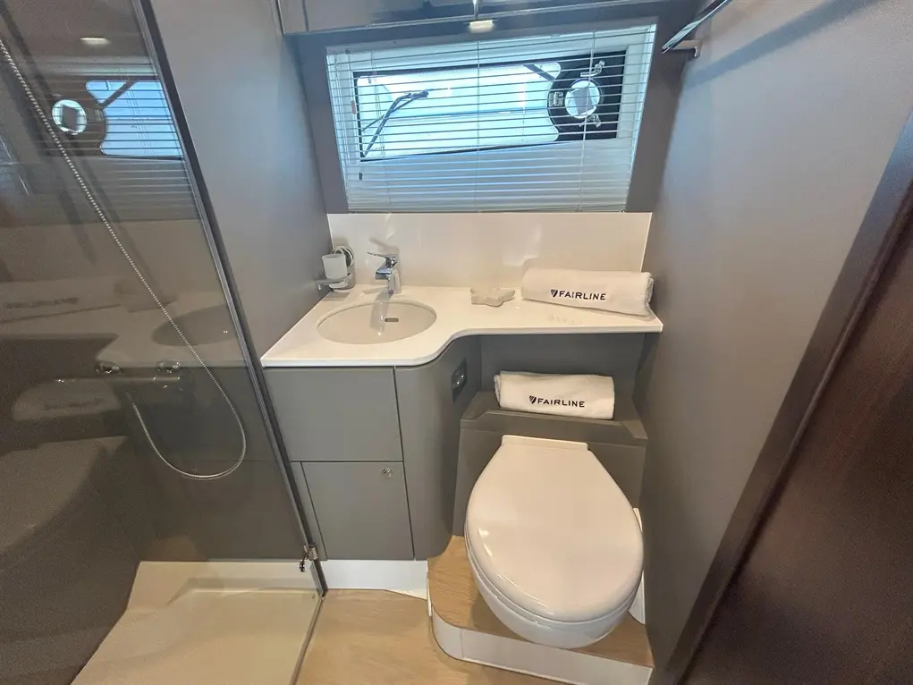 Compact boat bathroom featuring a sink, shower, toilet, and neatly arranged towels with "FAIRLINE" branding.